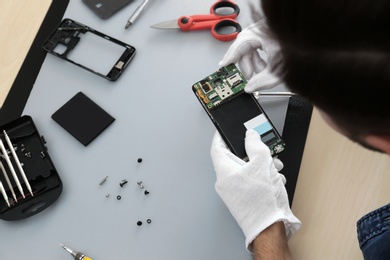 Technician repairing broken smartphone at table, closeup