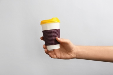 Woman holding takeaway paper coffee cup on light background