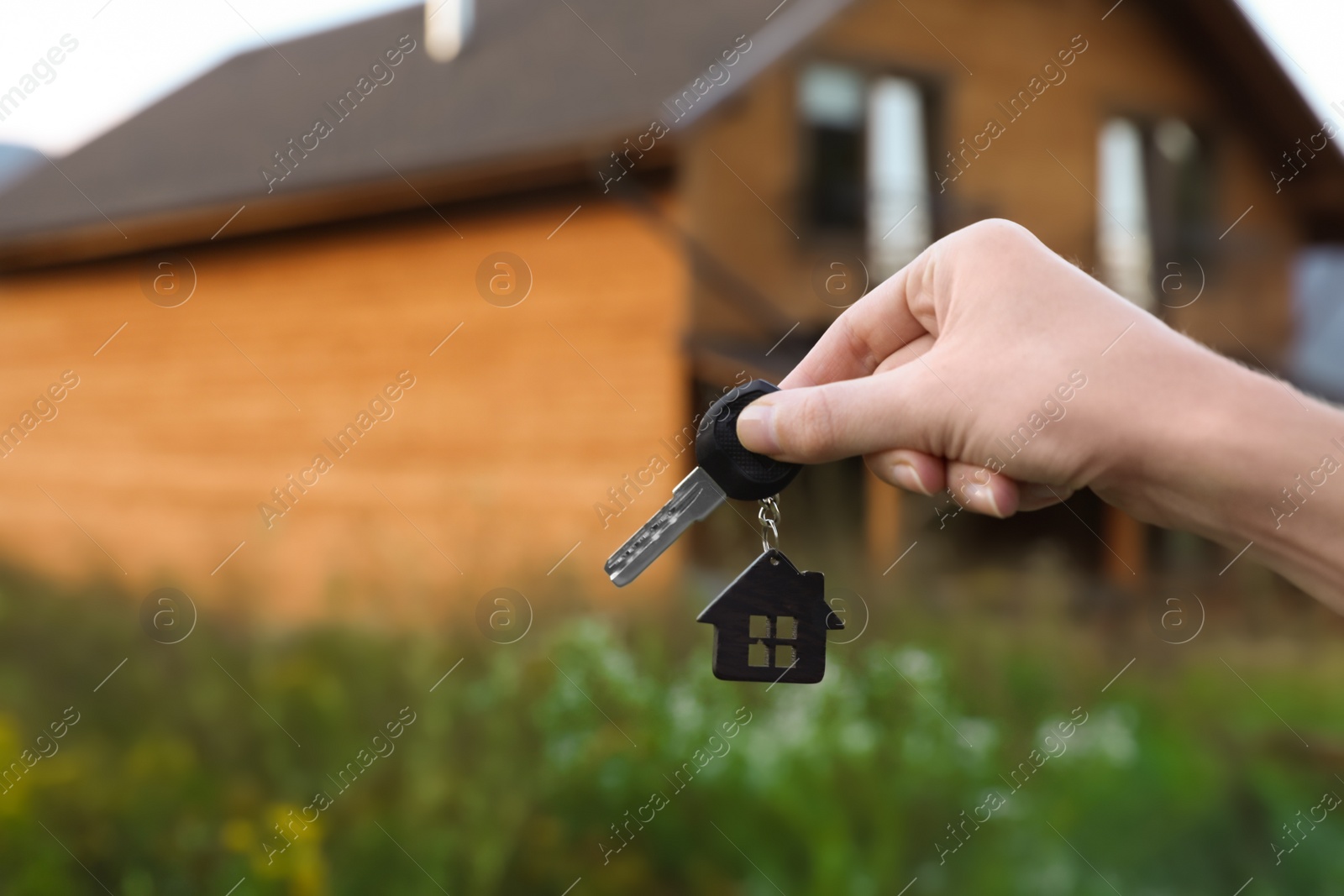 Photo of Real estate agent holding key and blurred house on background. Focus on hand