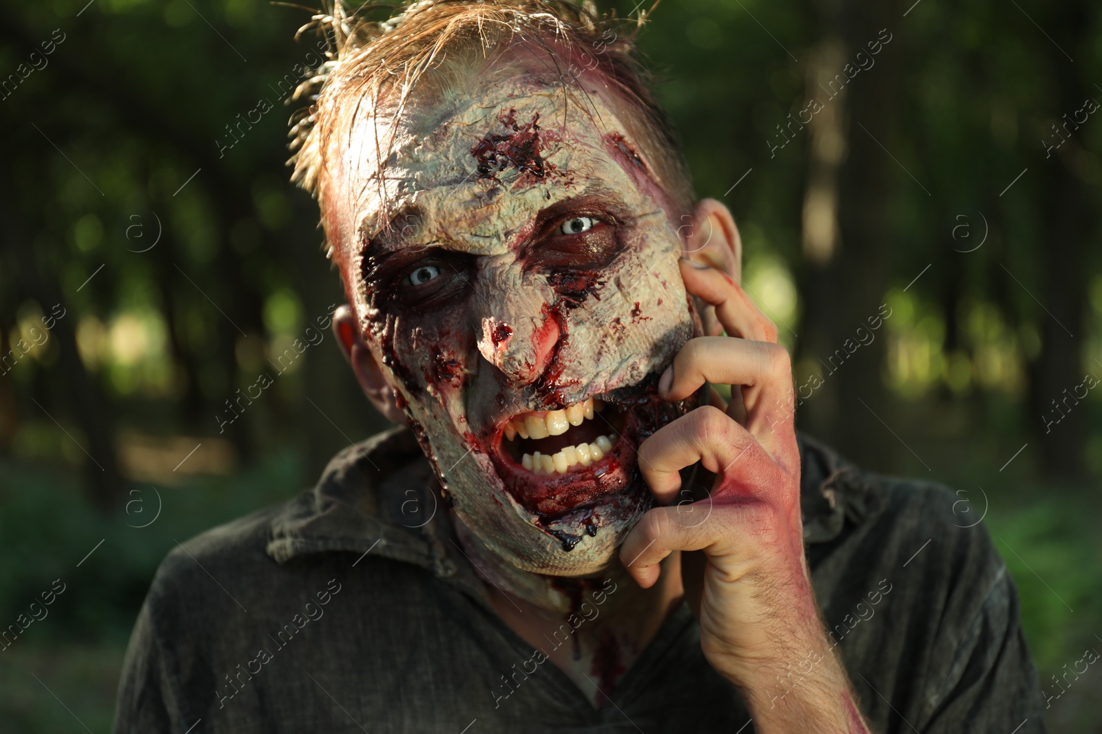 Photo of Scary zombie with bloody face outdoors, closeup. Halloween monster