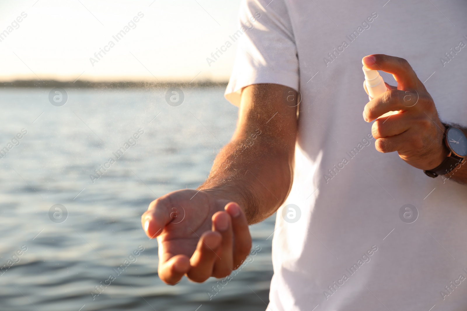 Photo of Man using insect repellent near sea on sunny day, closeup