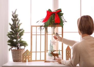 Woman creating Christmas composition inside of vintage wooden lantern on window sill indoors