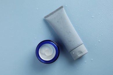 Moisturizing cream in tube and jar on light blue background with water drops, top view