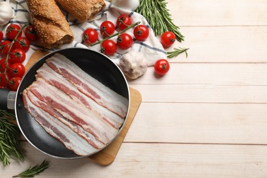 Slices of raw bacon in frying pan and fresh products on wooden table, flat lay. Space for text