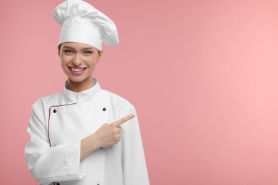 Photo of Happy chef in uniform pointing at something on pink background, space for text