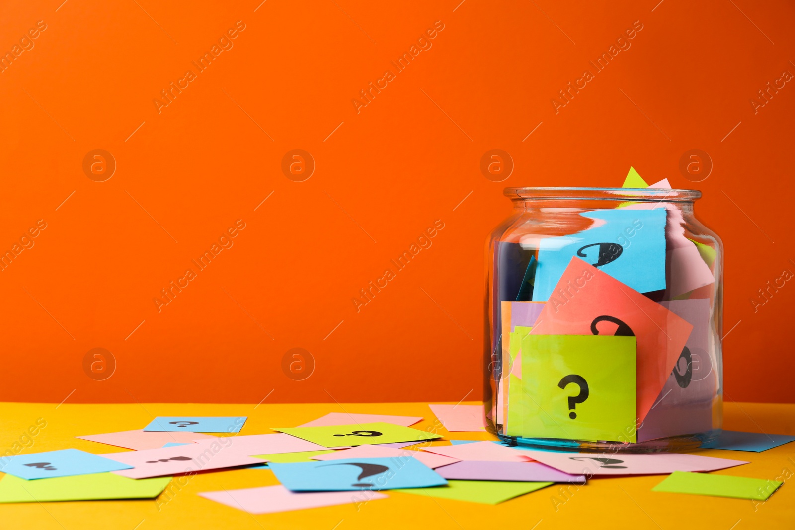 Photo of Colorful cards with question marks in glass jar on orange background. Space for text