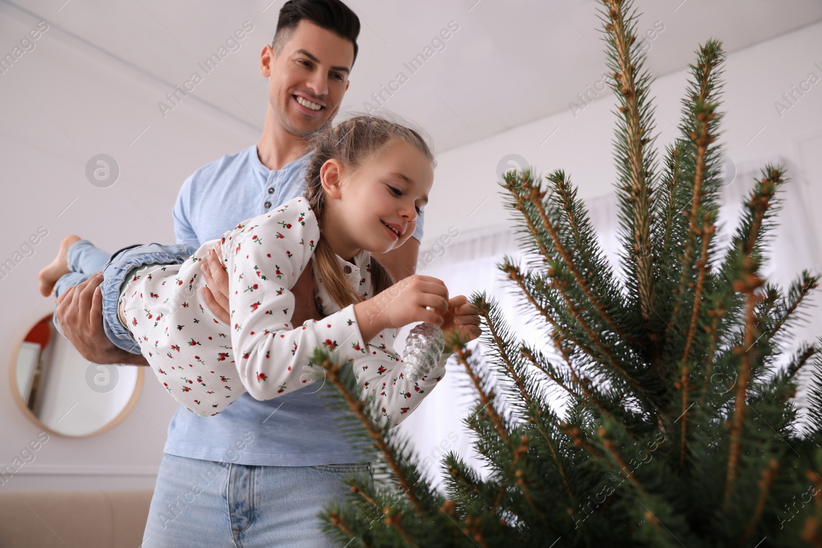 Photo of Father with his cute daughter having fun while decorating Christmas tree indoors