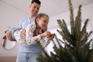 Photo of Father with his cute daughter having fun while decorating Christmas tree indoors