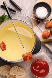 Photo of Fondue pot, forks with fried meat pieces, ketchup and other products on grey textured table, flat lay