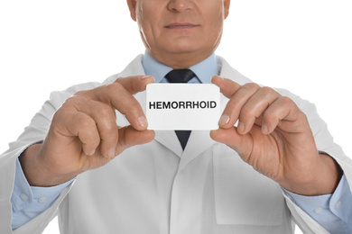 Photo of Doctor holding business card with word HEMORRHOID on white background, closeup