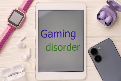 Photo of Tablet with phrase Gaming Disorder and devices on white wooden table, flat lay. Addictive behavior