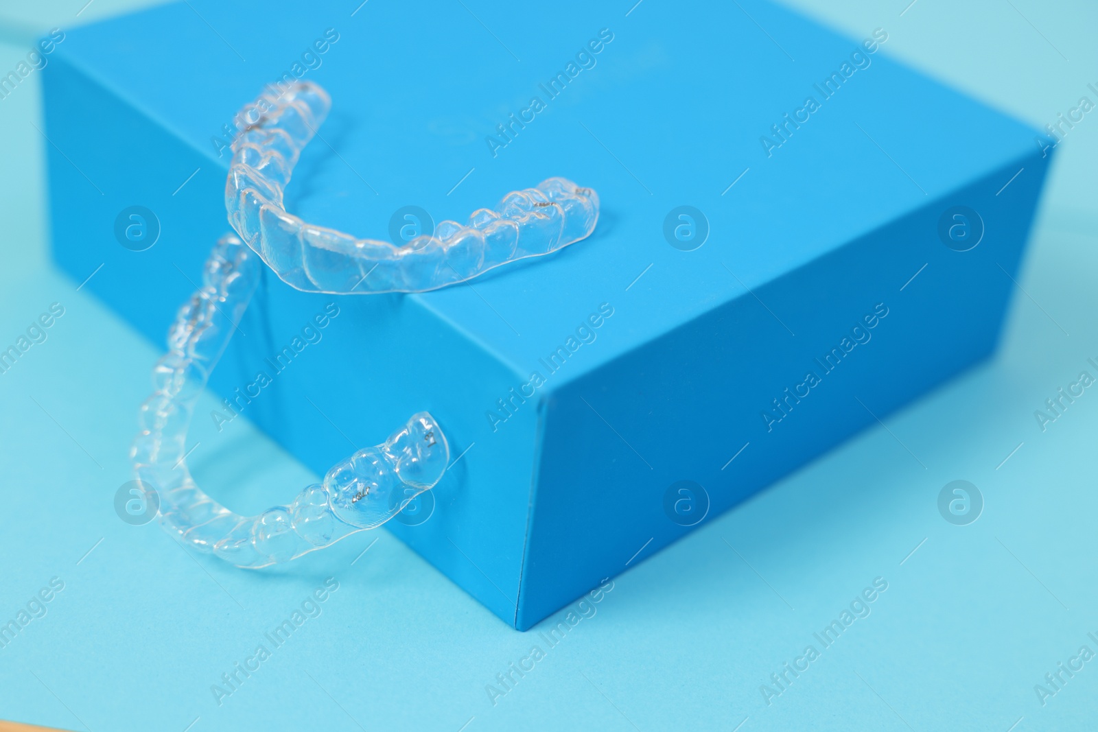 Photo of Transparent dental aligners on light blue background, closeup. Space for text