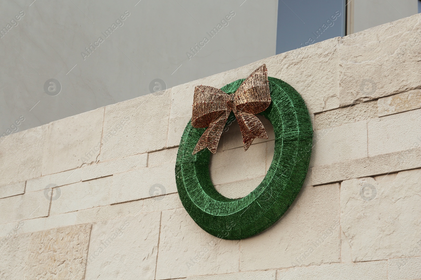Photo of Beautiful Christmas wreath with shiny bow hanging on wall outdoors