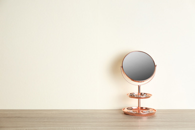 Small mirror and jewelry on wooden table near light wall. Space for text