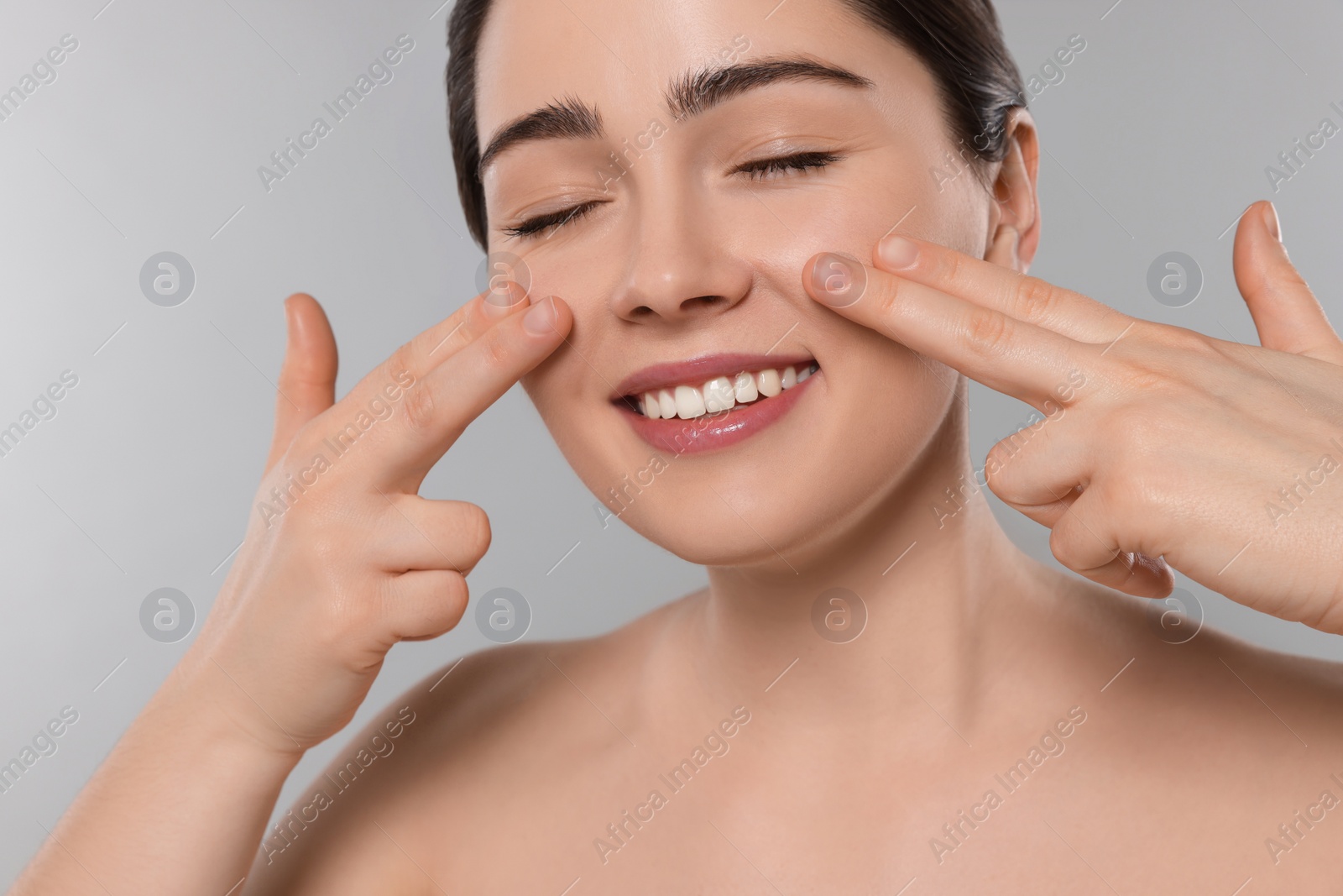 Photo of Young woman massaging her face on grey background