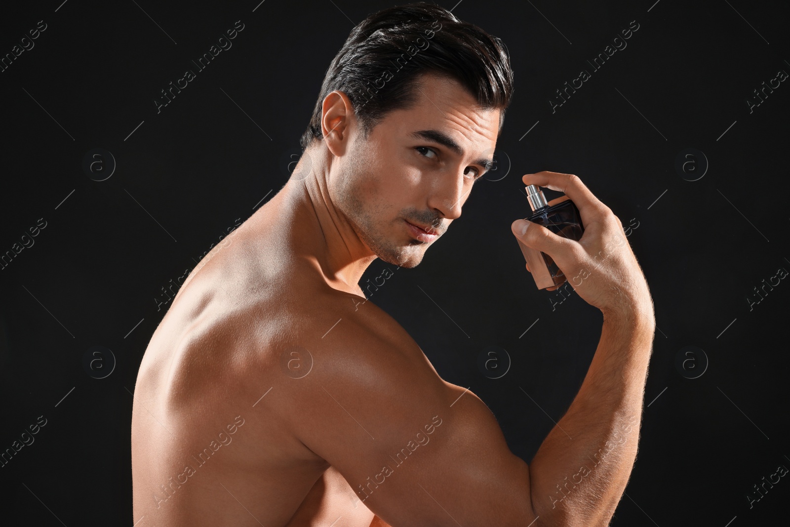 Photo of Handsome young man using perfume on black background