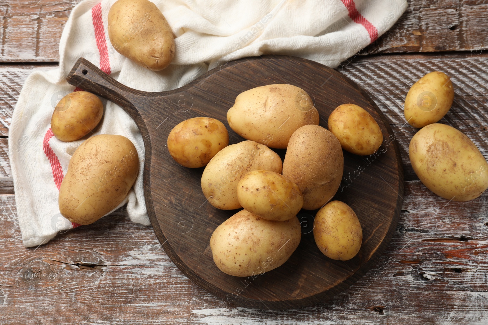 Photo of Raw fresh potatoes and cutting board on wooden table, top view