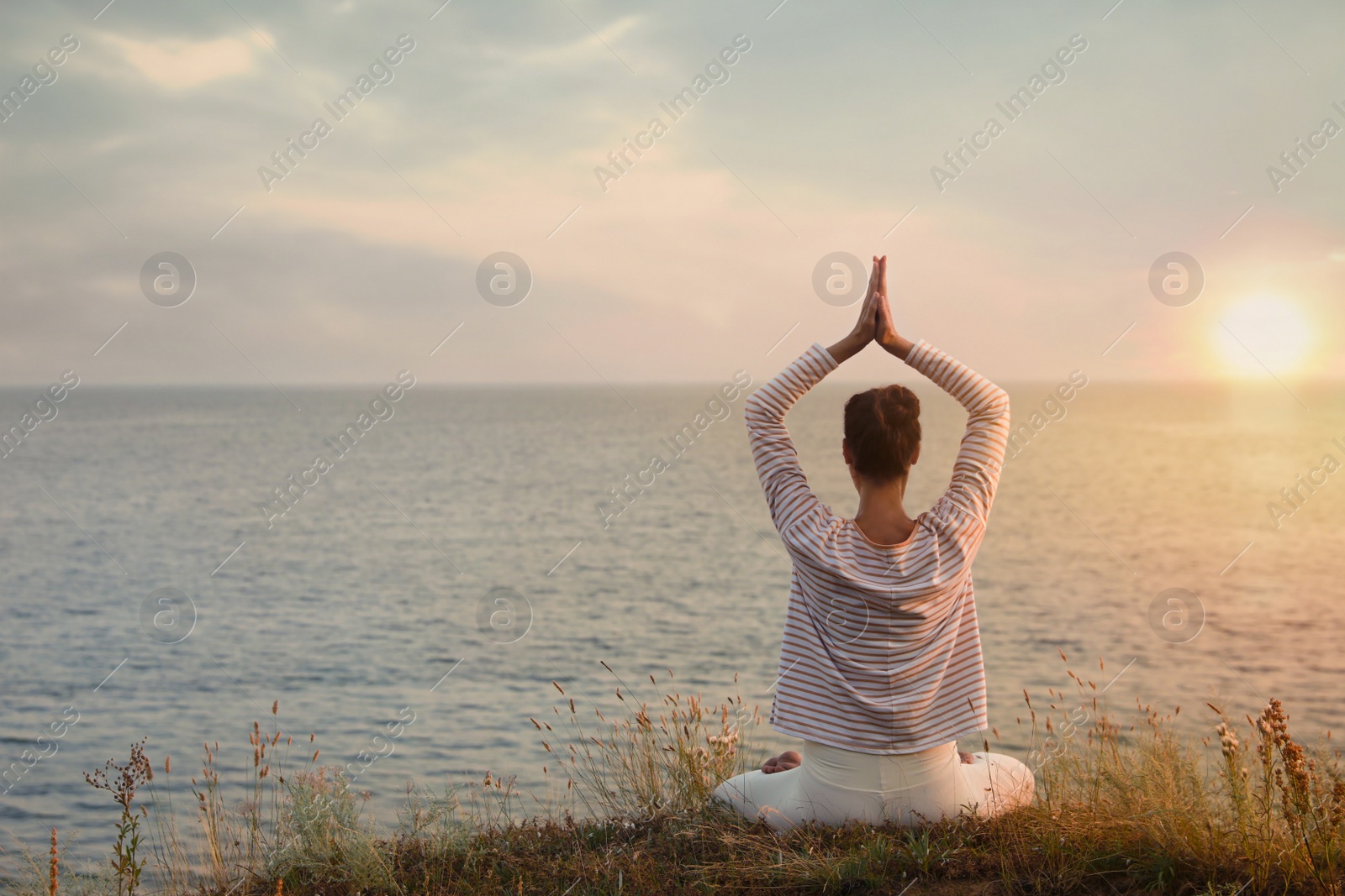 Photo of Woman meditating near sea, back view. Space for text