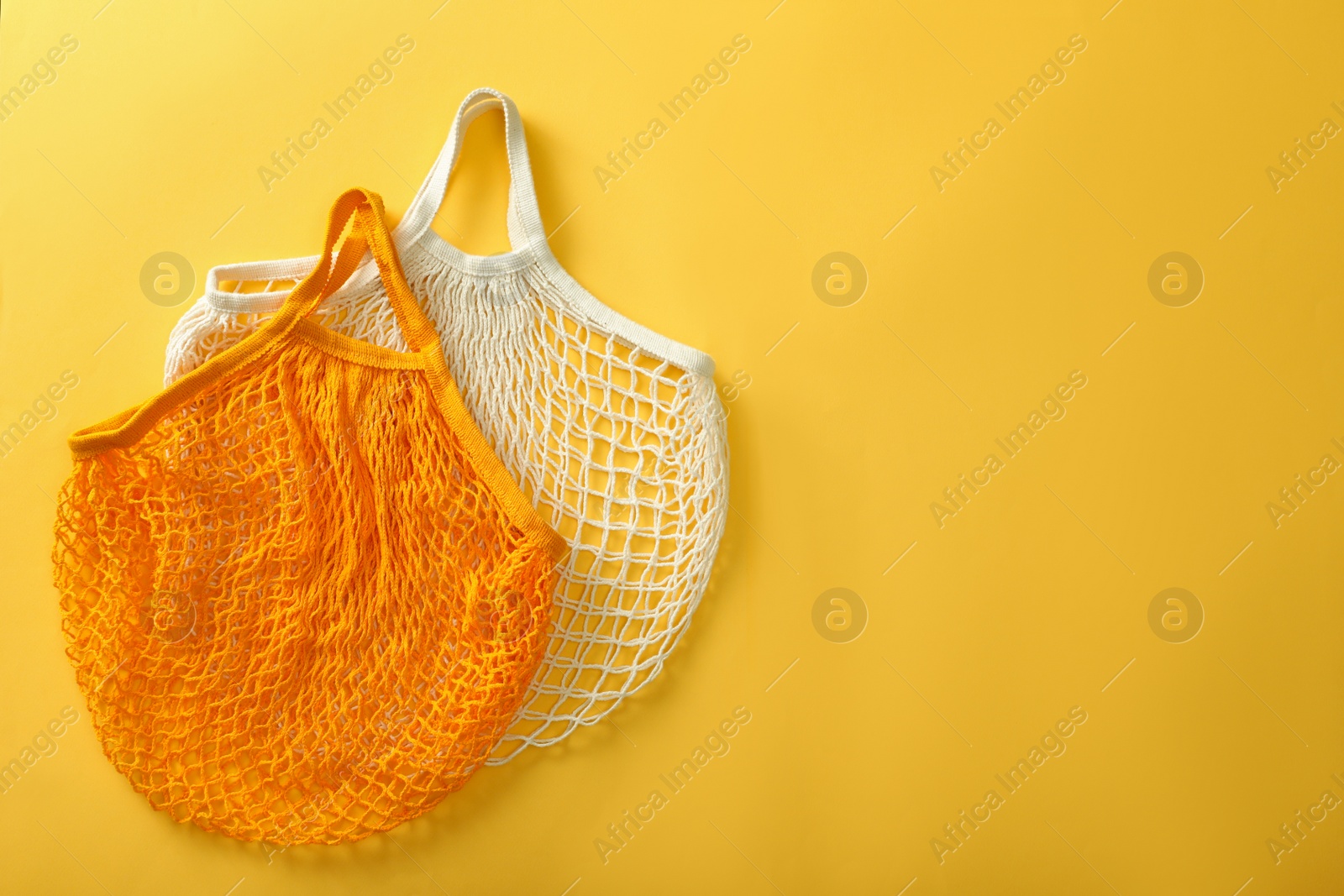 Photo of Empty net bags on yellow background, flat lay. Space for text