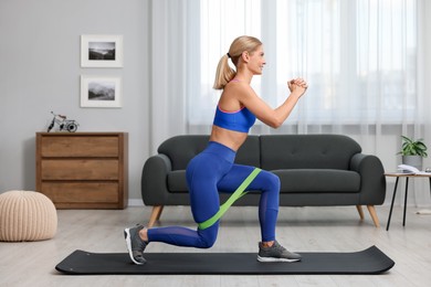 Photo of Athletic woman doing exercise with fitness elastic band on mat at home