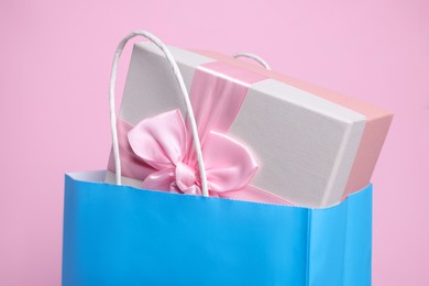Light blue paper shopping bag with gift box on pink background, closeup