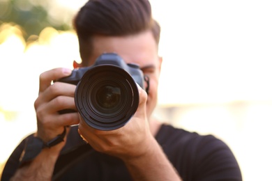 Photographer taking picture with professional camera in countryside, focus on lens