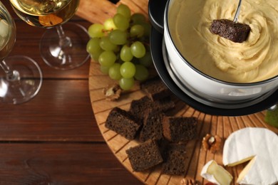 Photo of Dipping piece of bread into fondue pot with melted cheese on table with snacks, flat lay