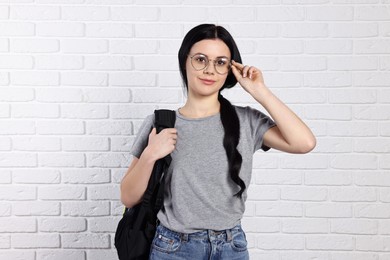 Photo of Student with backpack near white brick wall