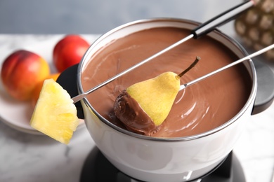 Photo of Dipping pear into pot with chocolate fondue on table, closeup