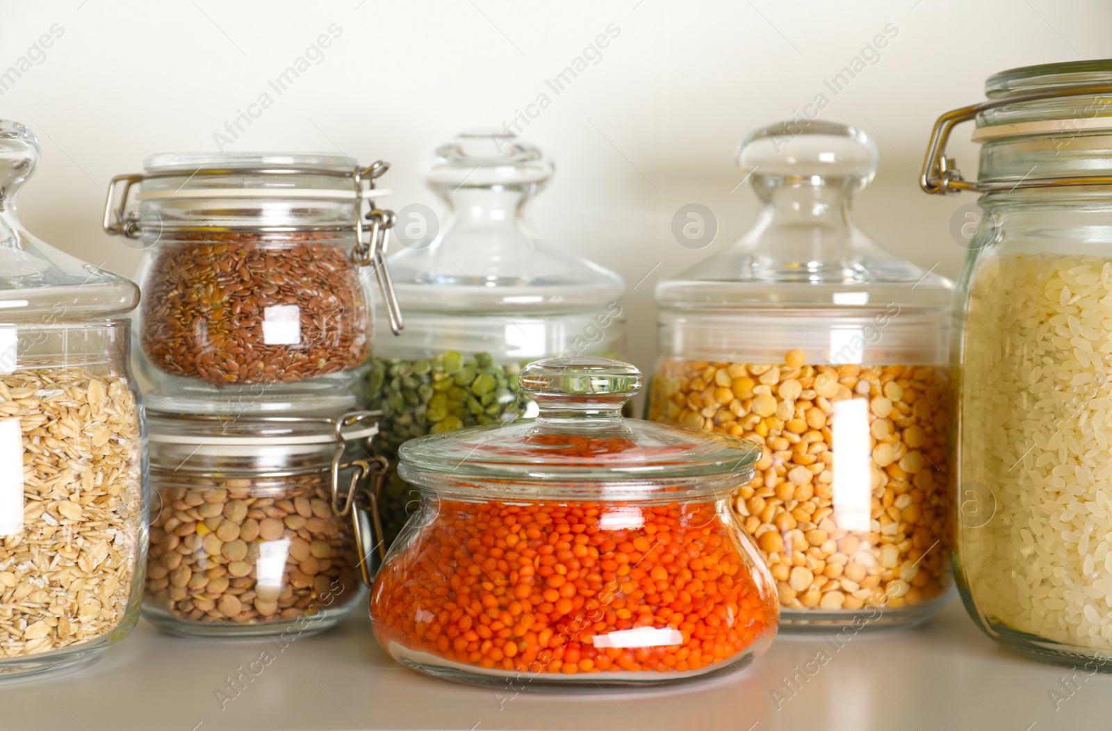 Photo of Different types of legumes and cereals in jars on table. Organic grains