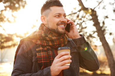 Man with cup of coffee talking on smartphone in morning outdoors