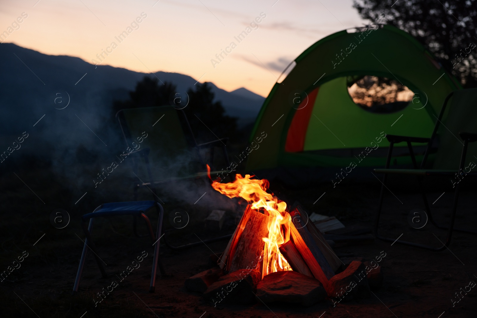 Photo of Beautiful bonfire and folding chairs near camping tent outdoors in evening