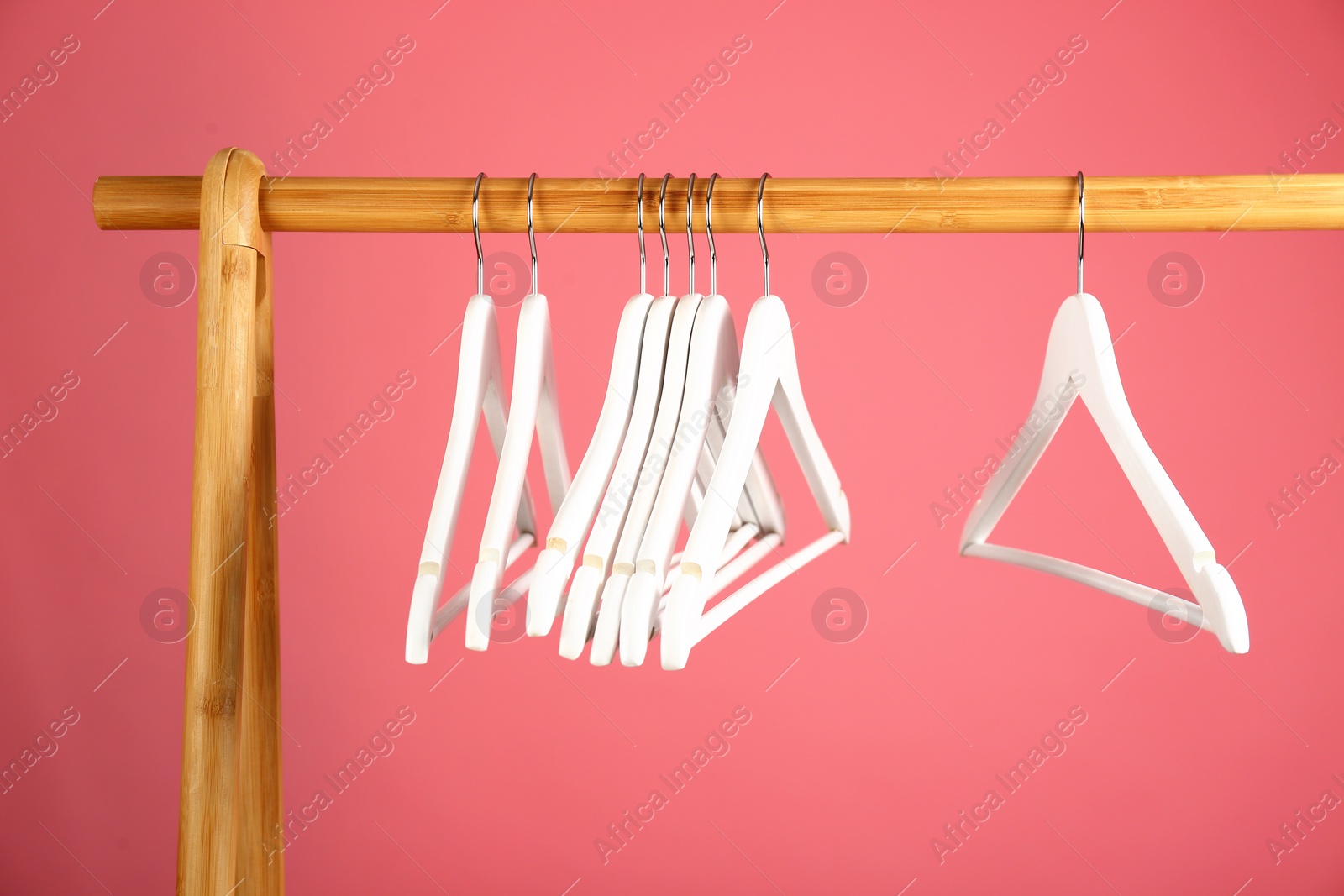 Photo of Empty clothes hangers on wooden rack against color background