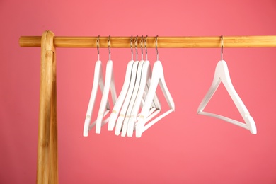 Photo of Empty clothes hangers on wooden rack against color background