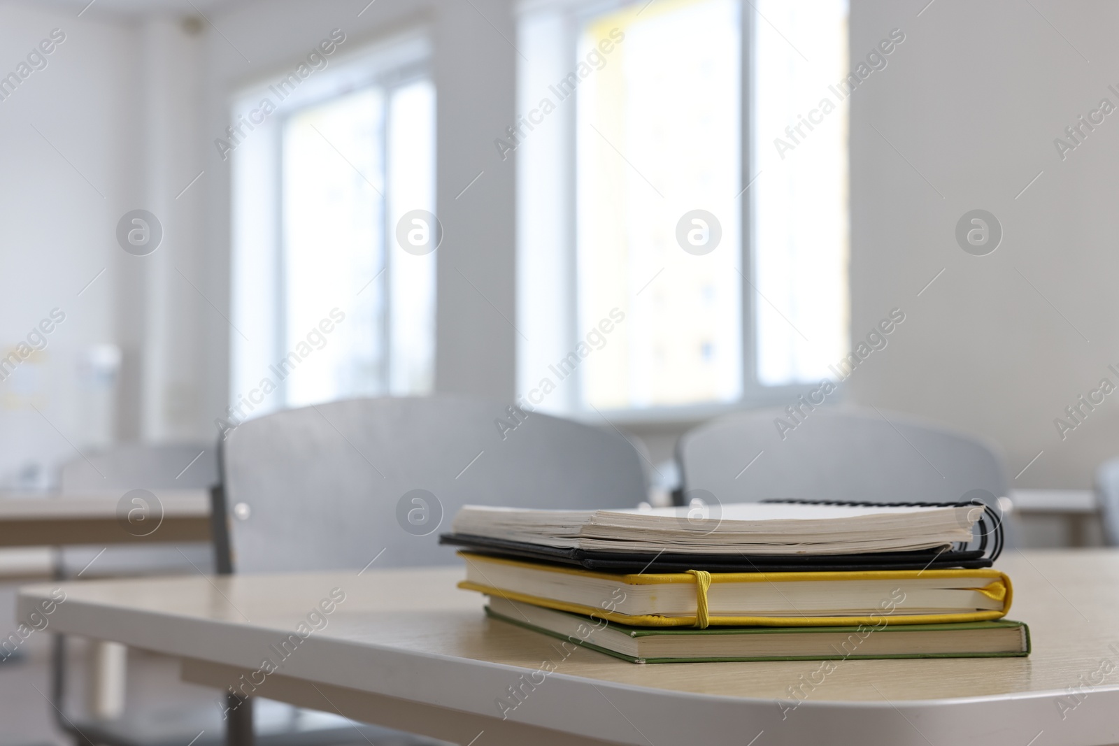 Photo of Stack of notebooks on wooden desk in empty classroom. Space for text