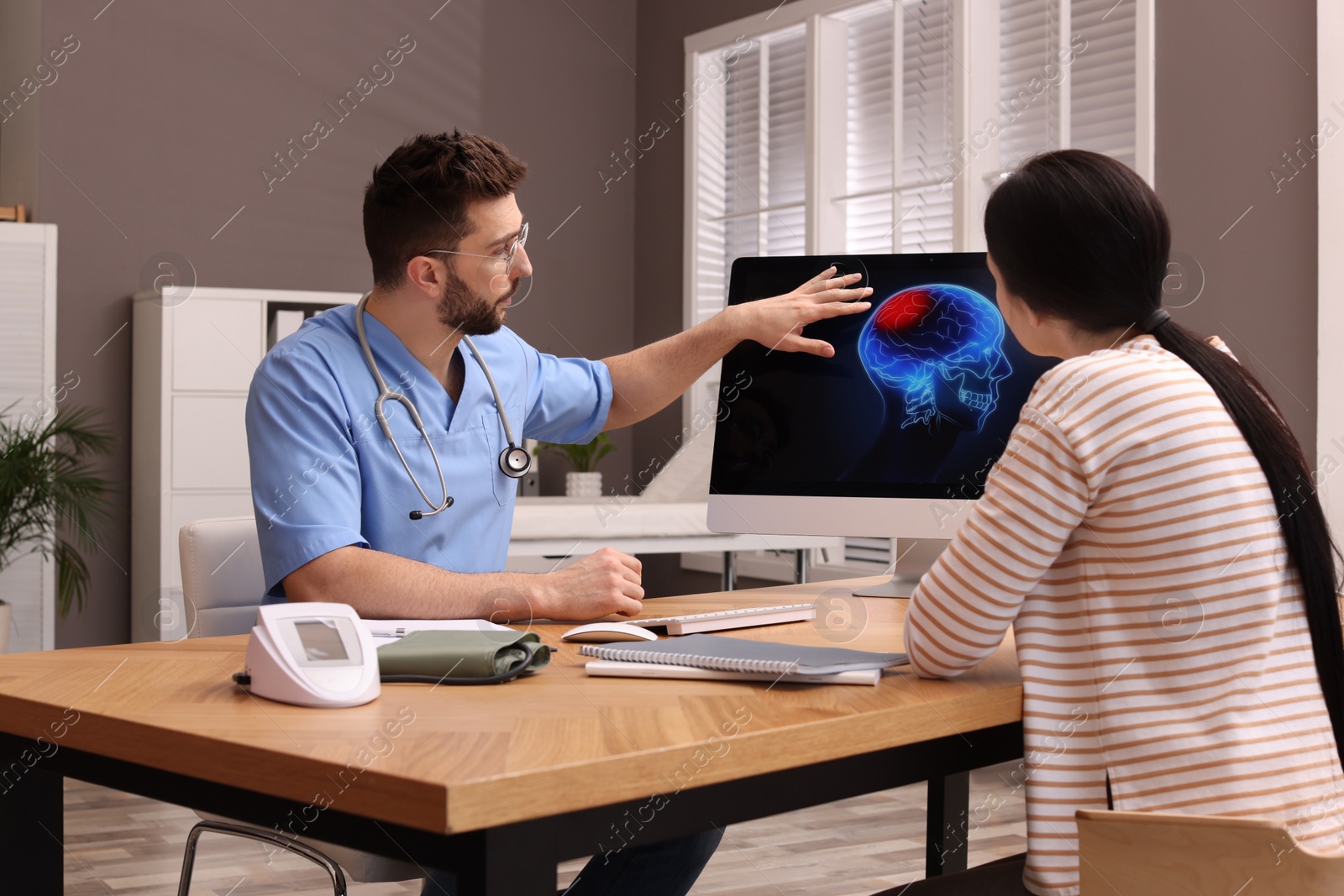 Photo of Neurologist showing brain scan to young woman in clinic