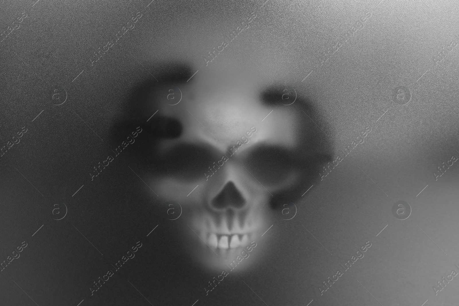 Photo of Silhouette of creepy ghost with skull behind cloth. Black and white effect