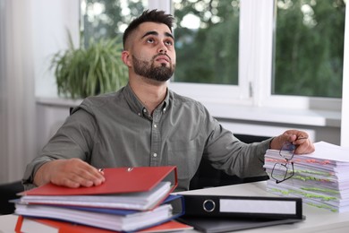 Overwhelmed man sitting at table with documents in office