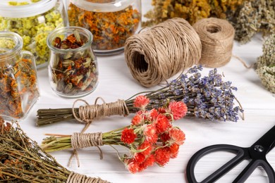 Photo of Bunches of dry flowers, different medicinal herbs and spools on white wooden table