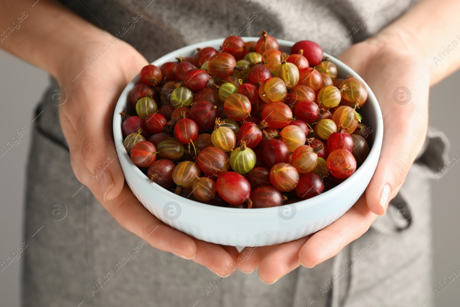 Photo of Woman holding bowl full of ripe gooseberries, closeup