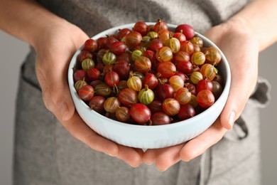 Woman holding bowl full of ripe gooseberries, closeup