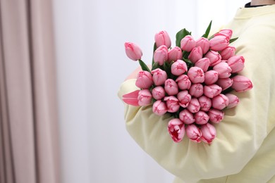 Photo of Woman holding bouquet of pink tulips indoors, closeup. Space for text