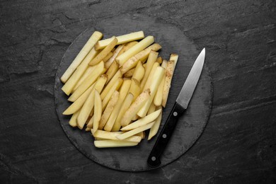 Photo of Cut raw potatoes with knife on black table, top view