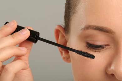 Photo of Woman applying mascara on grey background, closeup