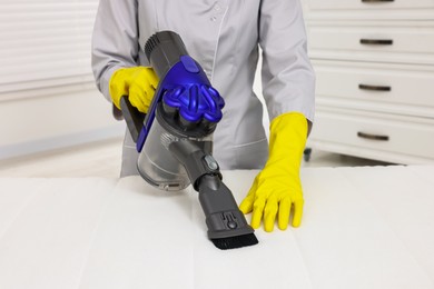 Photo of Woman in gloves disinfecting mattress with vacuum cleaner indoors, closeup