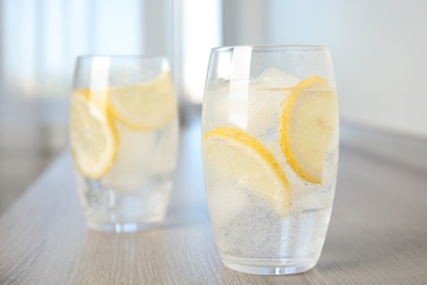 Soda water with lemon slices and ice cubes on wooden table indoors. Space for text