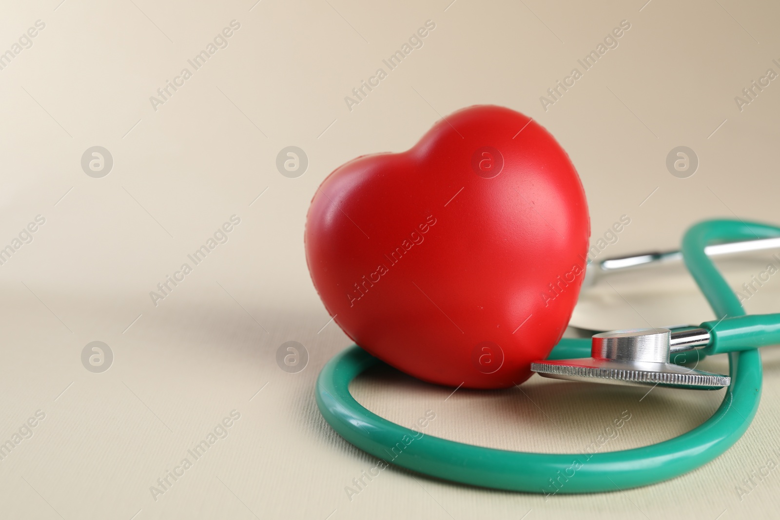 Photo of Stethoscope and red heart on beige background. Space for text