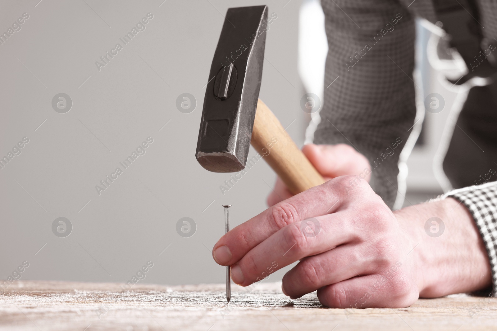 Photo of Professional repairman hammering nail into wooden board indoors, closeup