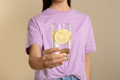 Photo of Woman with tasty lemon water on beige background, closeup