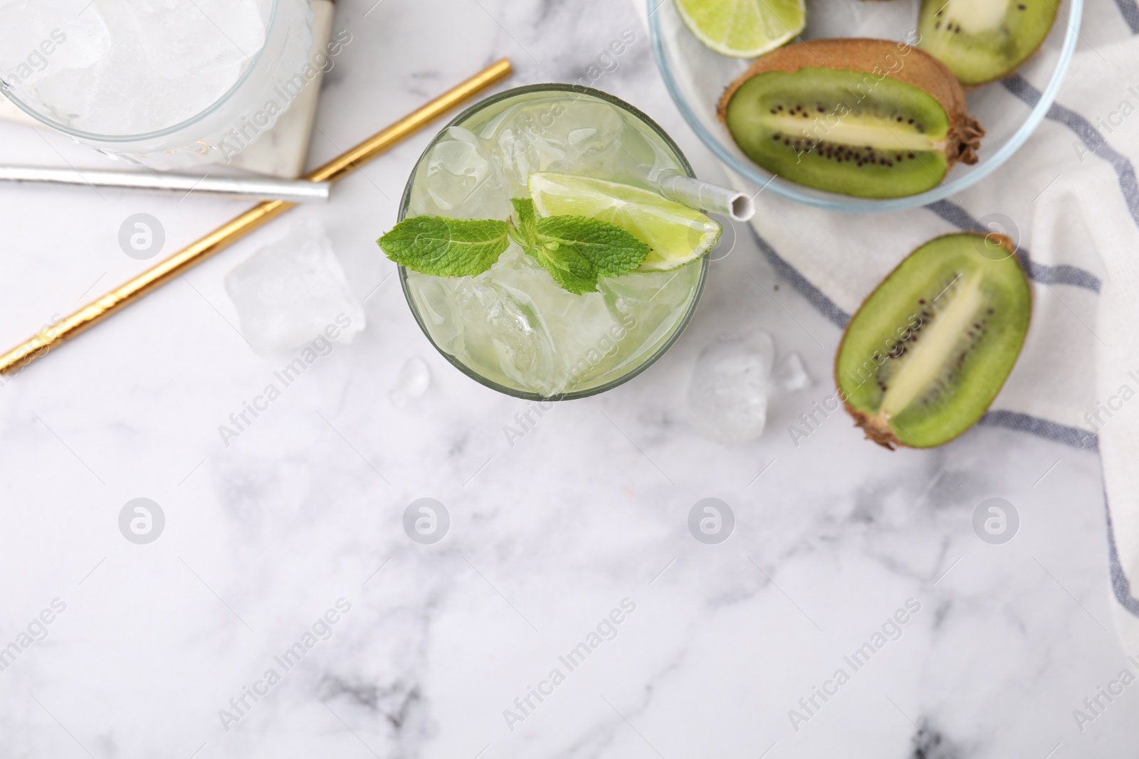 Photo of Glass of refreshing drink with lime and cut kiwi on white marble table, flat lay. Space for text